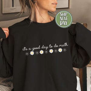 May include: Black sweatshirt with the phrase "it's a good day to do math" in white script, decorated with small daisy graphics. The sweatshirt is a solid black color.