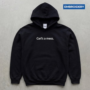 May include: Black hooded sweatshirt with a front pocket and the text "Carl's a mess." in white. The sweatshirt has a drawstring hood and is made of a soft material. The word "EMBROIDERY" is in a blue rectangle in the upper right corner.