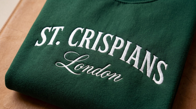 Może przedstawiać: Ciemnozielona bluza w kolorze lasu z białym haftowanym napisem ST. CRISPIANS pogrubioną czcionką szeryfową wielkimi literami, z wyrazem London napisanym poniżej białą kursywą w obszarze klatki piersiowej.