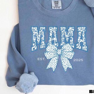 Elevate your style with this Custom Comfort Colors Mama Est Sweatshirt, a perfect blend of comfort and elegance. Designed with a Chinoiserie Blue Toile De Jouy pattern, this Coquette Bow Sweatshirt brings a timeless and feminine touch to any outfit. Whether you're looking for a girly aesthetic crewneck or a unique Mother's Day Gift, this Comfort Colors 1566 sweatshirt is a stylish and meaningful choice for moms.
Featuring a blue ribbon sweater design, this ribbon sweatshirt is inspired