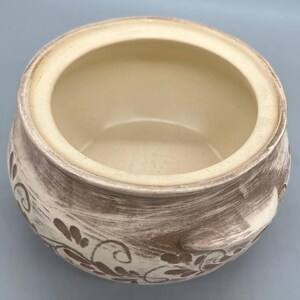 May include: A ceramic bowl with a cream-colored interior and a textured, brown and cream exterior. The bowl features a floral design and is suitable for serving or display.