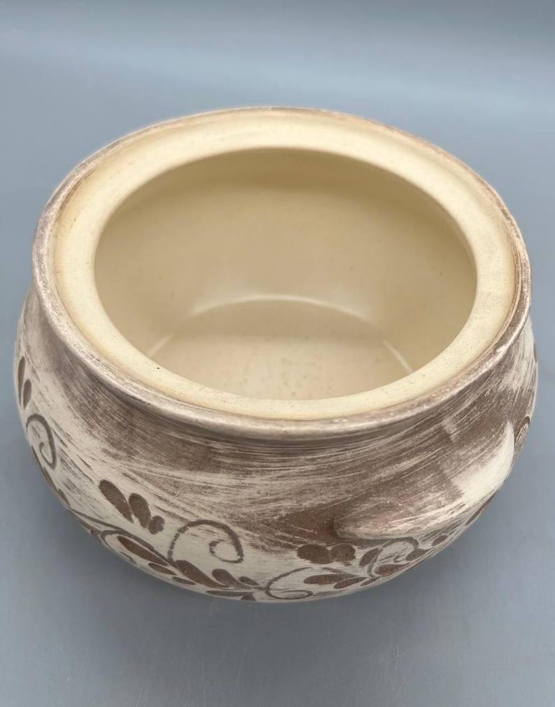 May include: A ceramic bowl with a cream-colored interior and a textured, brown and cream exterior. The bowl features a floral design and is suitable for serving or display.