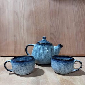 May include: A blue and white speckled teapot and two matching mugs. The teapot has a rounded body and a spout on the side. The mugs have a rounded shape and a handle on the side.