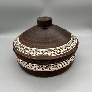 May include: A brown ceramic serving dish with a lid. The dish has a white floral design around the rim.
