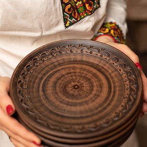 Puede incluir: Una pila de platos de cerámica marrón con un diseño decorativo alrededor del borde. Los platos son hechos a mano y tienen un aspecto rústico.