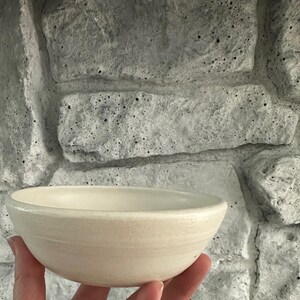 May include: A small, white ceramic bowl with a slightly rounded rim. The bowl is smooth and has a subtle sheen.