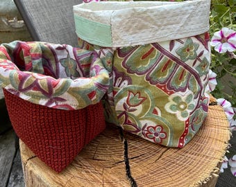 May include: Two fabric storage baskets. The larger basket has a paisley pattern in green, burgundy, and cream, with a mint green accent. The smaller basket is red with a textured pattern. Both are on a wooden stump.
