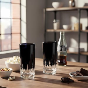 Puede incluir: Dos vasos altos negros con base de cristal tallado sobre una mesa de madera. Una botella de refresco, un cuenco de palomitas de ma&iacute;z y un cuenco de frutos secos tambi&eacute;n est&aacute;n sobre la mesa. Trozos de chocolate en un cuenco blanco.