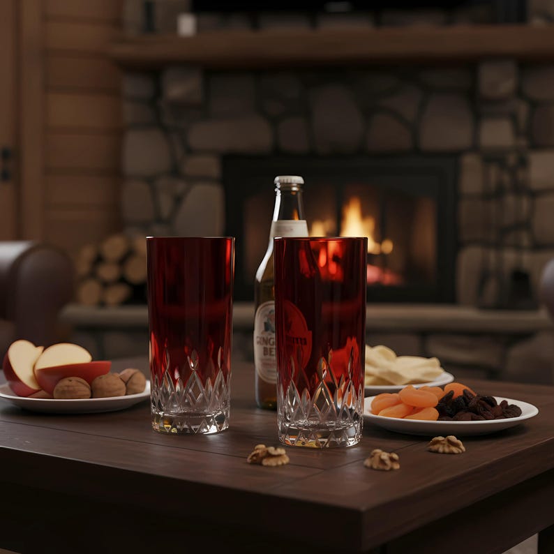 Puede incluir: Dos vasos altos de cristal rojo rub&iacute; con un dise&ntilde;o tallado en diamante est&aacute;n sobre una mesa de madera oscura. Una botella de cerveza y platos con aperitivos, incluyendo rodajas de manzana, nueces y fruta seca, tambi&eacute;n est&aacute;n sobre la mesa. Una chimenea con fuego c&aacute;lido est&aacute; al fondo.
