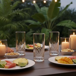 Puede incluir: Una mesa al aire libre con vasos altos y transparentes con un patr&oacute;n de diamantes, platos de fruta y velas encendidas. La escena es al aire libre con exuberante follaje verde y luces de cadena en el fondo.