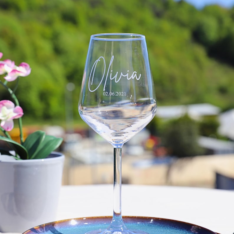 May include: A clear glass wine glass with the name "Olivia" and the date "02.06.2021" etched on the side.