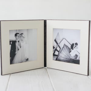 May include: A black and white photo album with two open pages. The left page shows a couple posing for a wedding photo. The right page shows a couple kissing on a staircase.