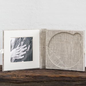 May include: A linen-covered photo album with a white matted photo of two hands clasped together. The album has a separate compartment for a CD or DVD.