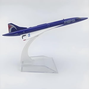 May include: A blue and white model of a Concorde airplane with the Pepsi logo on the side. The model is mounted on a clear plastic stand. The tail fin has a red, white, and blue design. The model is a collectible item.
