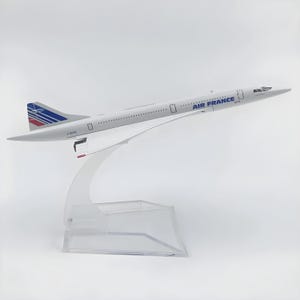 Può includere: Modello bianco di aereo Concorde Air France, con dettagli blu e logo Air France. Il modello è esposto su un supporto in acrilico trasparente. La coda presenta strisce blu, bianche e rosse. Oggetto da collezione.