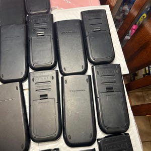 May include: A collection of ten black graphing calculators. The calculators are all in the same style and have a similar design. The calculators are arranged in a row, with the top row having five calculators and the bottom row having five calculators.