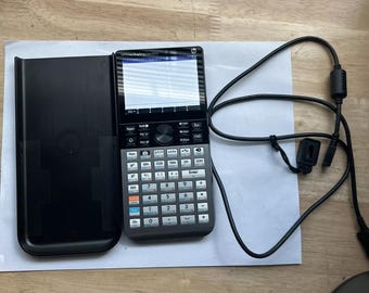 Könnte beinhalten: Ein schwarz-silberner Grafikrechner mit Bildschirm und Tastatur. Der Rechner befindet sich in einem schwarzen Etui und hat ein schwarzes Kabel daran.