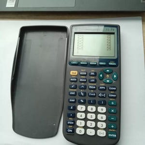 May include: A black and gray TI-73 graphing calculator with a screen displaying a mathematical equation. The calculator has a variety of buttons, including numbers, operations, functions, and a clear button.