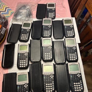 May include: A collection of 12 black and silver TI-84 Plus graphing calculators in protective cases. The calculators have a black and white screen and a variety of buttons.