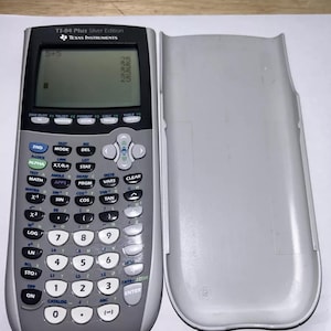May include: A silver TI-84 Plus Silver Edition calculator with its gray protective cover. The calculator displays the equation 5+5 on the screen. The calculator has numerous buttons for various mathematical functions.