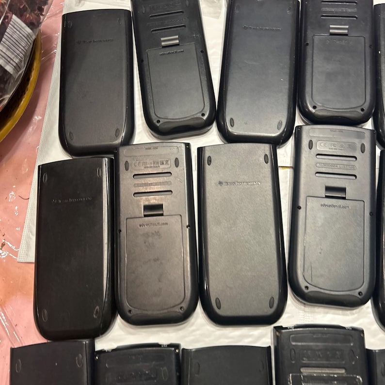 May include: A collection of ten black graphing calculators. The calculators are all the same model and have a similar design. They have a rectangular shape with a small screen and a keypad.