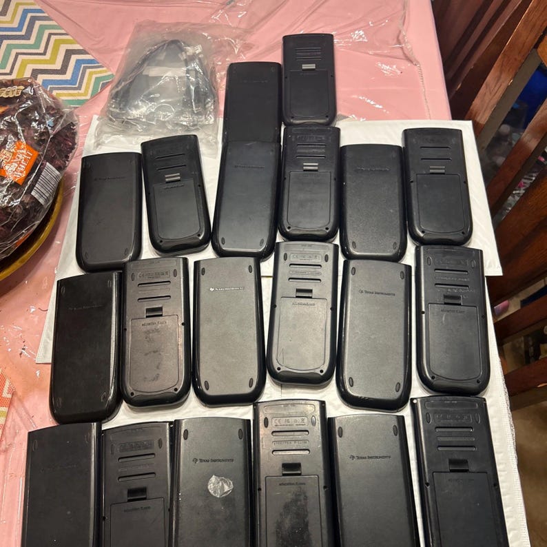 May include: A collection of 18 black graphing calculators, some with the brand name "Texas Instruments" visible on the back.