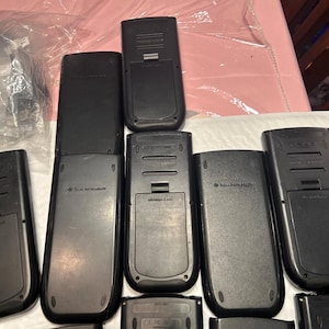 May include: A collection of eight black calculators with various branding and model numbers. The calculators are arranged in a row, with some stacked on top of others.