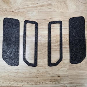 Puede incluir: Cuatro almohadillas y marcos adhesivos negros texturizados est&aacute;n dispuestos sobre una superficie de madera clara. Dos son rectangulares y dos tienen forma de marco con esquinas redondeadas. Las almohadillas tienen un aspecto moteado.