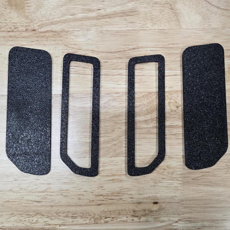 Puede incluir: Cuatro almohadillas y marcos adhesivos negros texturizados est&aacute;n dispuestos sobre una superficie de madera clara. Dos son rectangulares y dos tienen forma de marco con esquinas redondeadas. Las almohadillas tienen un aspecto moteado.