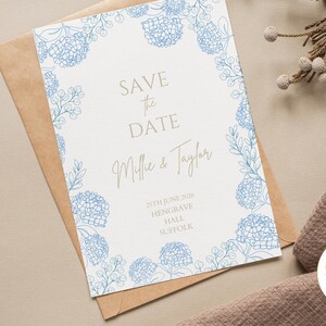 May include: A blue and white save the date card with a floral border. The text reads "Save the Date" with the names "Mille & Taylor" and the date "25th June 2020". The location is listed as "Hengrave Hall, Suffolk".