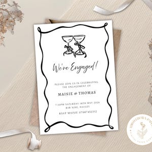 May include: White engagement announcement card with black text and a decorative border. The card features the words "We're Engaged!" and details for Maisie & Thomas's celebration. The card is set against a neutral background with floral and ribbon accents.