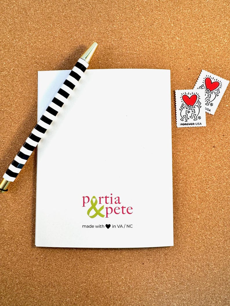 Peut inclure: Une carte blanche avec un stylo ray&eacute; noir et blanc dessus. La carte porte un logo vert et rose qui dit "portia & pete" et "made with &hearts; in VA/NC".