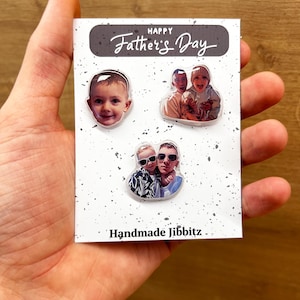 Op de afbeelding: Drie handgemaakte Jibbitz-bedels met foto's van een vader en zijn kinderen. De bedels zijn rond en hebben een witte achtergrond met een transparante plastic overlay. De tekst "Happy Father's Day" is gedrukt op een grijze achtergrond bovenaan de kaart. De tekst "Handmade Jibbitz" is gedrukt onderaan de kaart.
