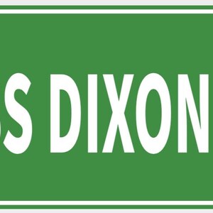 Pode incluir: Uma placa de rua verde com o texto branco "USS DIXON DR". A placa tem uma borda branca e é montada com dois rebites. A placa é retangular.