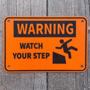 May include: Orange warning sign with black text that reads "WARNING WATCH YOUR STEP" with a black silhouette of a person falling down a set of stairs.