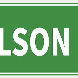 Pode incluir: Uma placa de rua verde com o texto branco "OLSON DR". A placa tem uma borda branca e é fixada com dois rebites. A placa retangular é um marcador rodoviário comum.