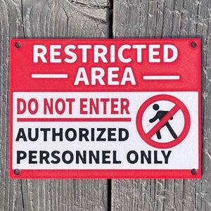 Può includere: Un cartello rosso e bianco con il testo "AREA RISERVATA - DIVIETO DI ACCESSO - PERSONALE AUTORIZZATO SOLO". Un cerchio rosso con una linea diagonale e una figura stilizzata che cammina è al centro del cartello.