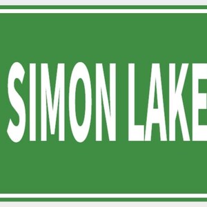 Pode incluir: Uma placa de rua verde com texto branco que diz "USS SIMON LAKE" e "DR" no canto superior direito. A placa tem uma borda branca e é montada com dois rebites.