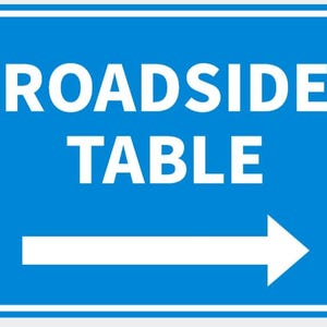 May include: A blue rectangular sign with the words "ROADSIDE TABLE" in white, and a white arrow pointing right. The sign has a white border and is secured with four silver rivets.