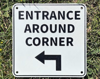 Señal de entrada en esquina con flecha direccional en blanco vibrante con letras negras para interiores y exteriores.