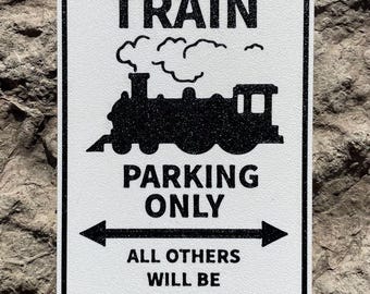 Può includere: Un cartello bianco con testo nero e una silhouette nera di un treno. Il cartello dice "Train Parking Only. All others will be side-tracked."