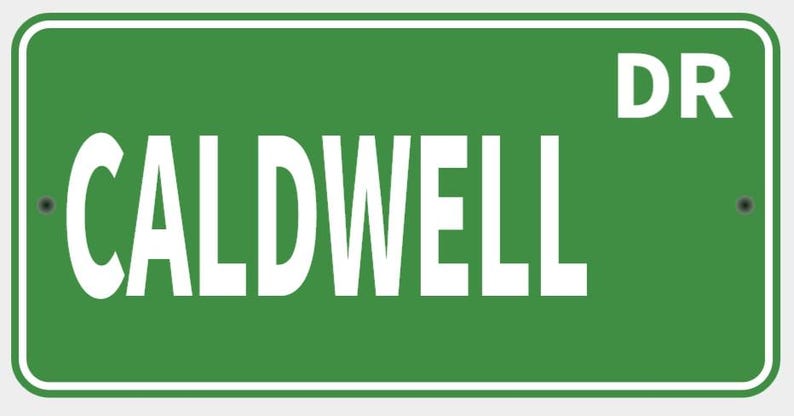 May include: A green street sign with white text that reads "CALDWELL DR". The sign has a white border and is mounted with two rivets. The sign is rectangular.
