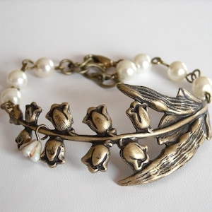 Puede incluir: Un delicado brazalete con un encanto de lirio de los valles de bronce con cuentas de perlas blancas.
