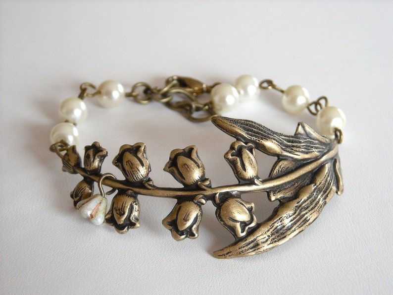 Puede incluir: Un delicado brazalete con un encanto de lirio de los valles de bronce con cuentas de perlas blancas.