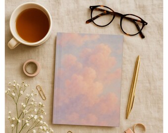 Peut inclure: Un carnet avec un motif de nuages roses et violets, un stylo doré et des lunettes écailles sont disposés sur une surface en lin neutre. Une tasse de thé, du ruban adhésif washi et une branche de fleurs blanches complètent la scène.