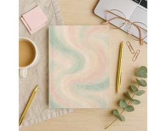 May include: A notebook with a pastel swirl design in shades of pink, green, and beige. The notebook is on a wooden surface, next to a cup of coffee, a laptop, glasses, and a gold pen.