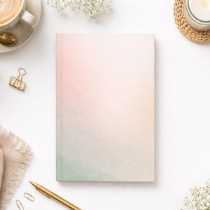 May include: A hardcover notebook with a pastel gradient cover, transitioning from pink to green. The image also includes a cup of coffee, a gold pen, paper clips, a candle, and floral accents, creating a serene, aesthetic composition.