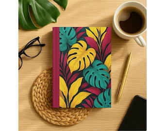 Peut inclure: Un journal à couverture rigide avec un motif de feuilles tropicales aux couleurs vives : teal, jaune et magenta. Le journal est posé sur une surface en bois avec une tasse de café, un stylo doré et un smartphone.