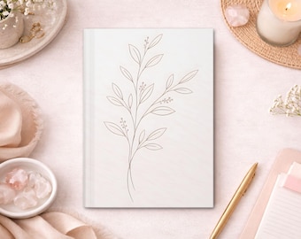 Peut inclure: Un journal crème avec un dessin au trait botanique délicat sur la couverture. L'image est mise en scène avec un stylo doré, une bougie allumée et de petits bols avec des cristaux, suggérant un thème de soins personnels et de journalisation.
