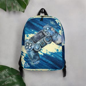 Op de afbeelding: Blauwe rugzak met een afbeelding in aquarel van een videogamecontroller. De controller is in tinten grijs en blauw, tegen een achtergrond van blauwe en gele penseelstreken. De rugzak heeft zwarte banden en een handvat aan de bovenkant.